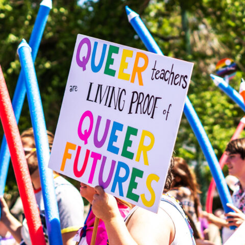 Utah Educators for Pride Group close up of sign "QUEER teachers are LIVING PROOF of QUEER FUTURES" in the LGBTQIA+ Pride Parade in Salt Lake City, Utah. June 04th, 2023 with multicolored pool noodle pencil props, and flags all unrecognizable.